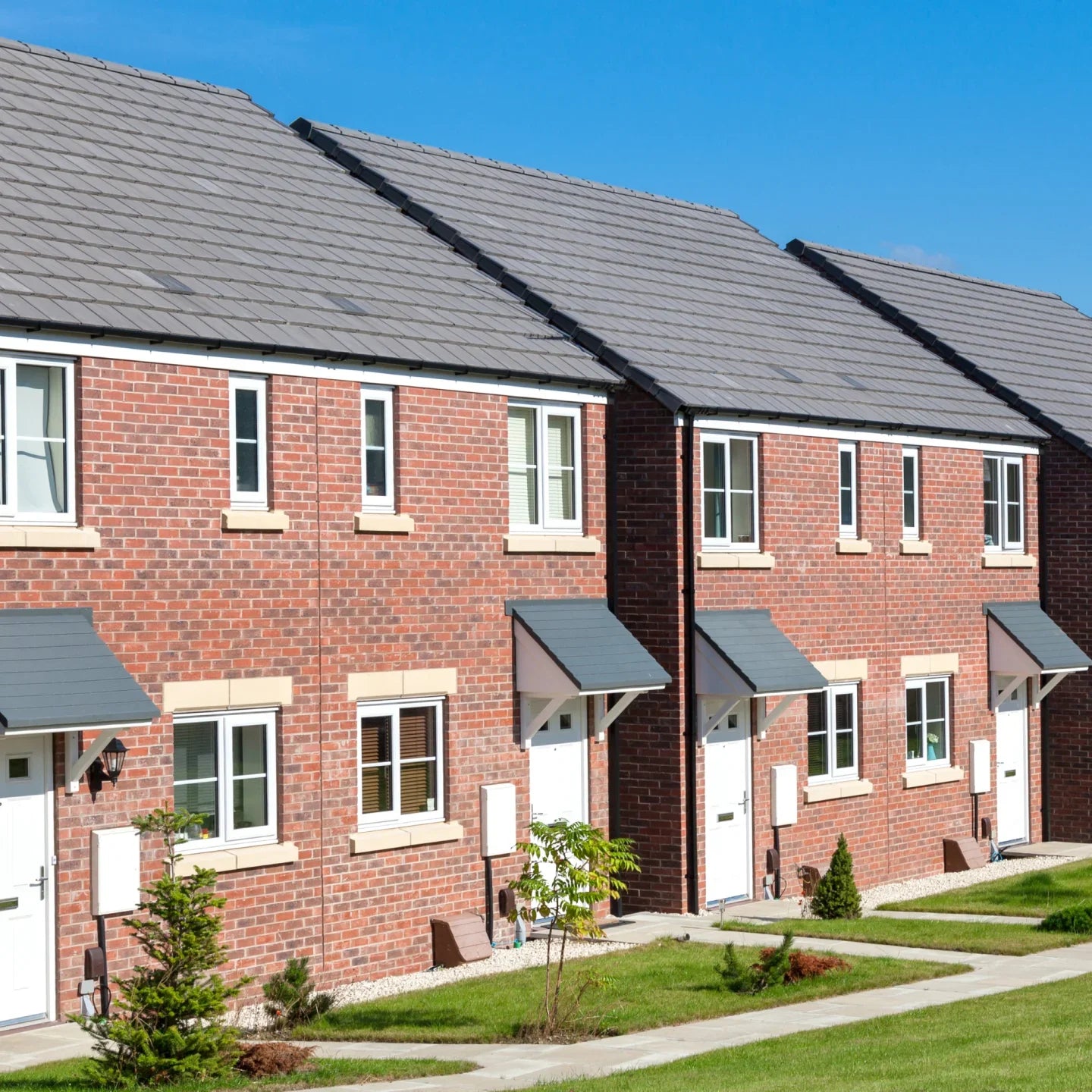 Row of red brick houses with gray roofs and white doors on a clear day.